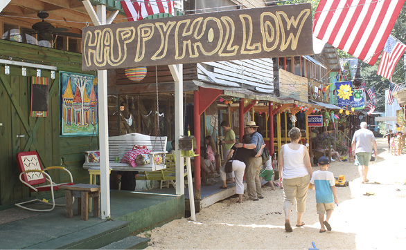 Brightly painted buildings with colorful signs, sitting areas, art, and banners. People are walking along the path, and American flags are displayed.