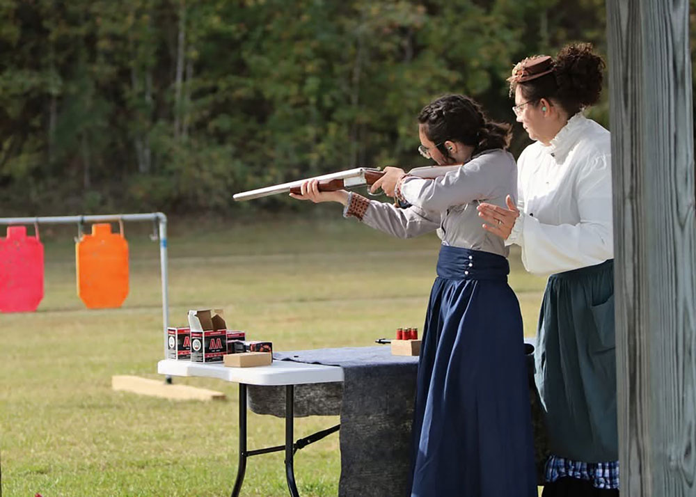 A person offers instruction to a young person at an outdoor shooting range.