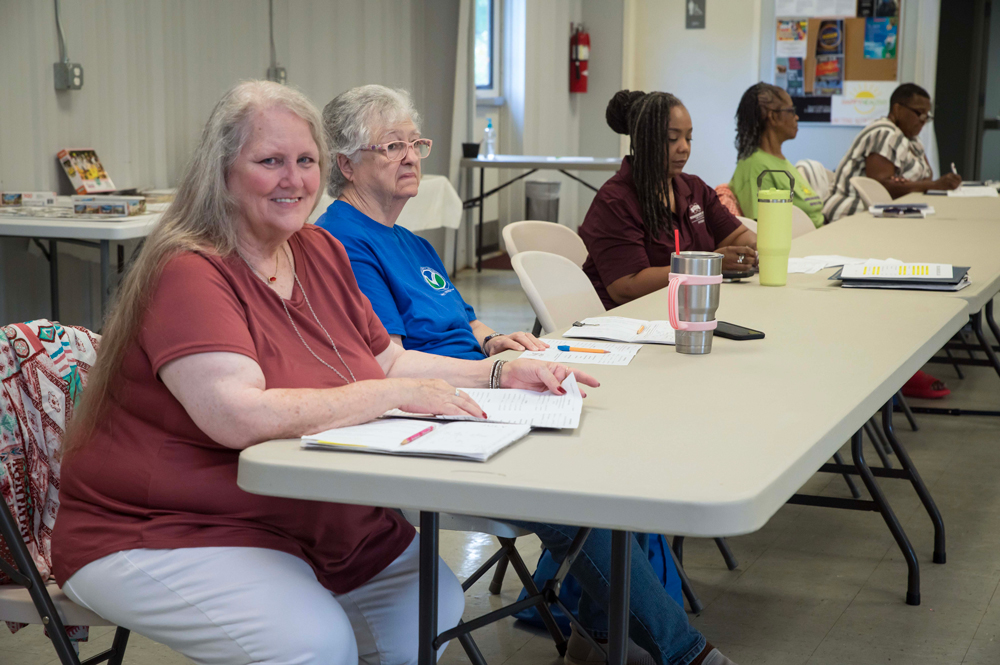 A woman smiling and seated at a conference table with other people.