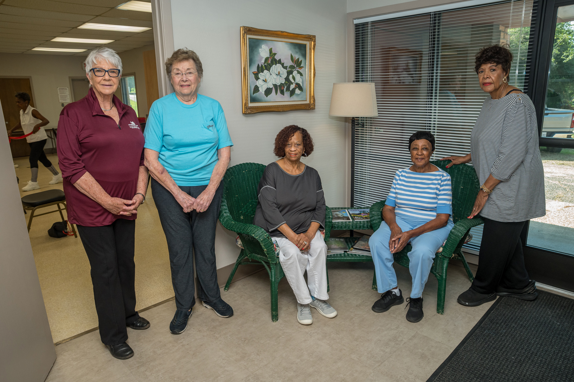 Five women in a row with 3 standing and 2 seated in chairs.