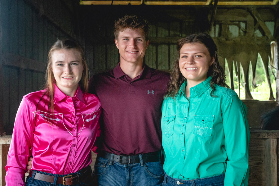 Three people standing in a barn, smiling.