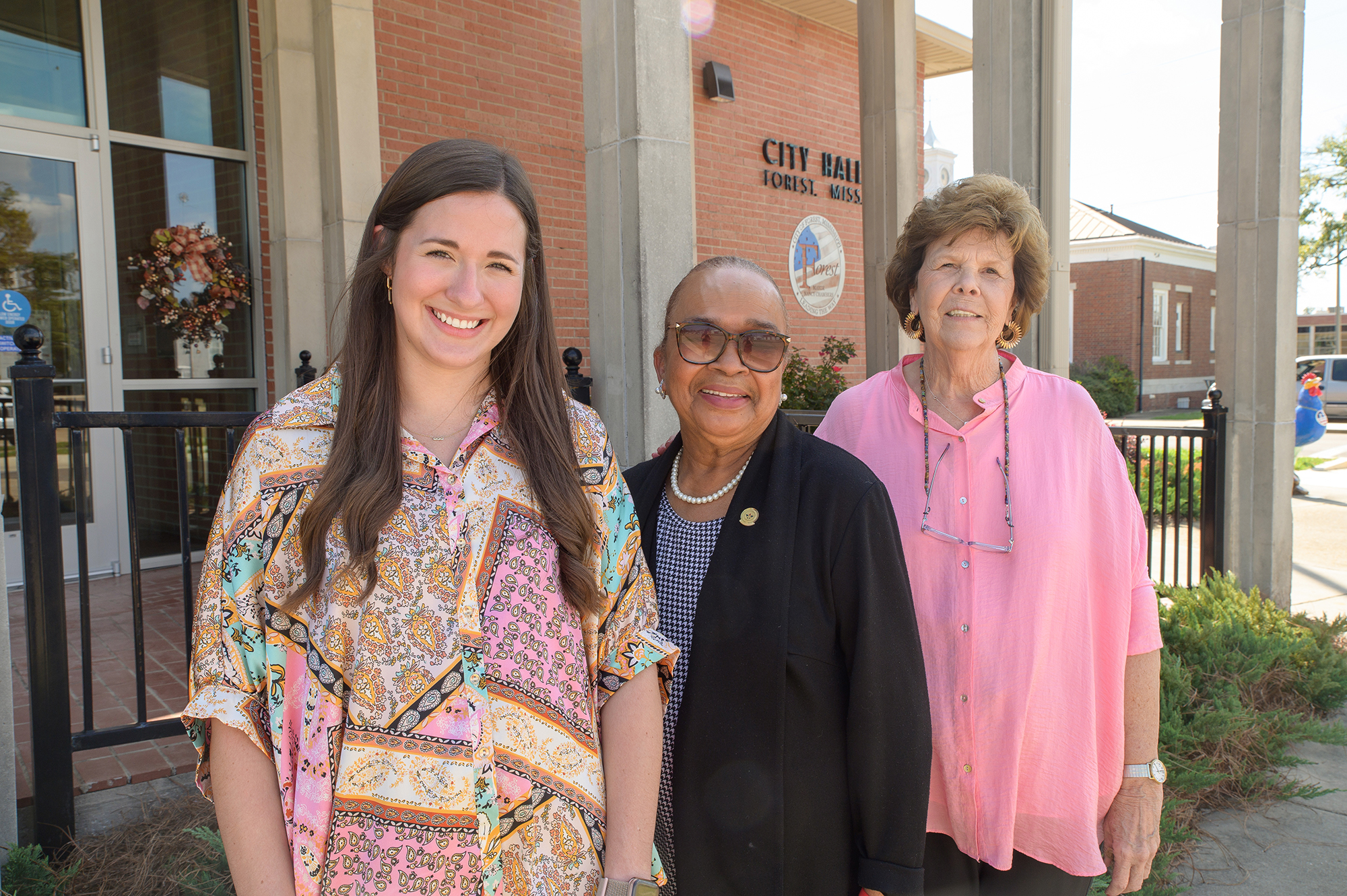 Three people stand in front of the city hall in Forest, MS.