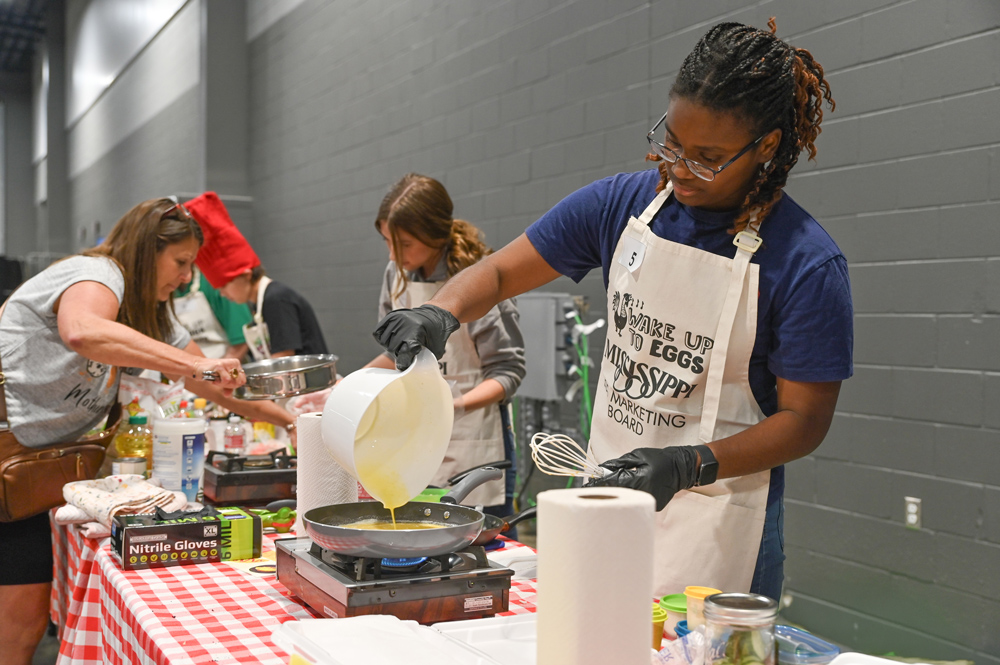 A young woman pours egg mixture into a pan.