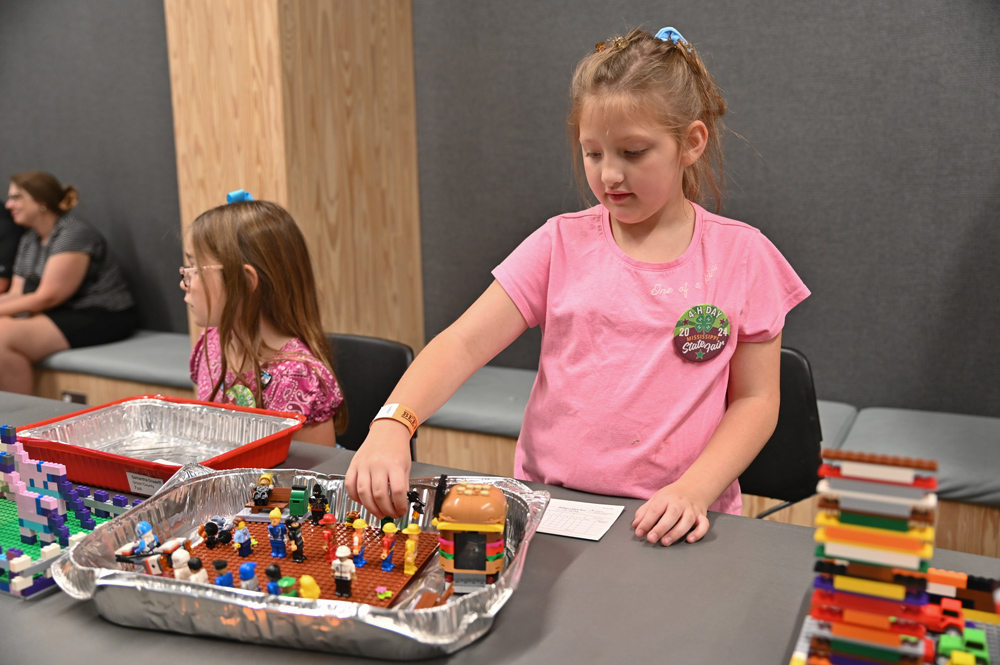 A child adds a LEGO piece to a LEGO creation in a tray.
