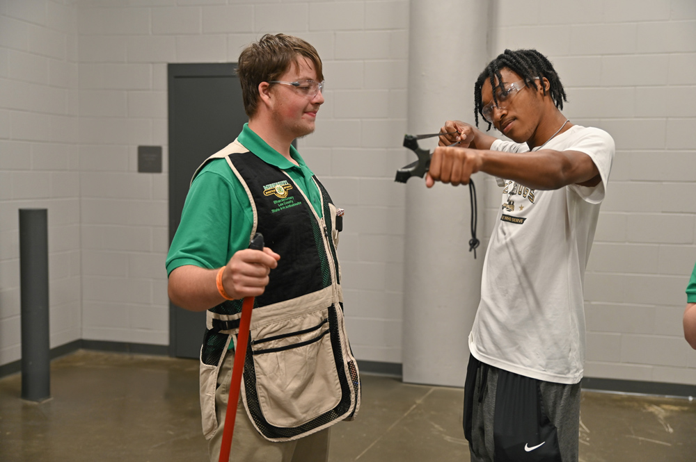 A student aims a slingshot as another student watches.