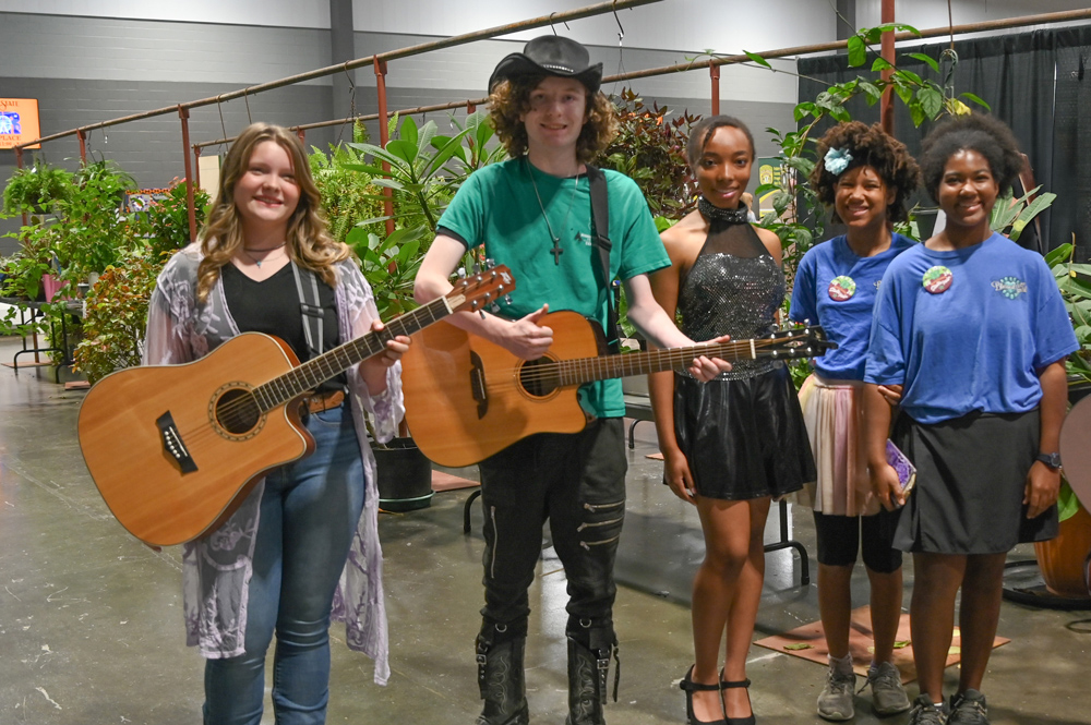 Two students, each holding a guitar, stand near a student in a party dress and two other students both wearing blue shirts. 