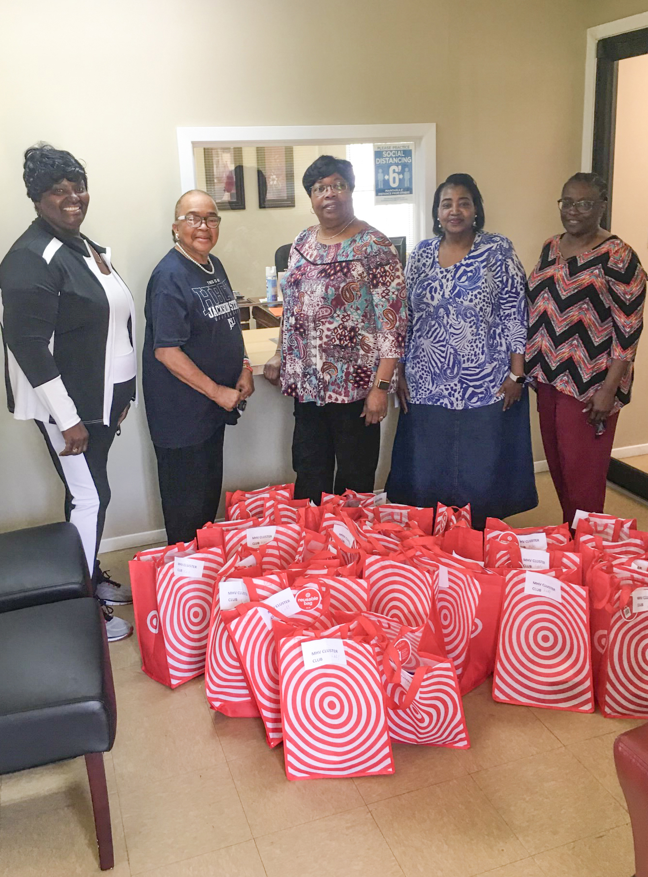 Five people stand behind a large group of red bags with white circles.