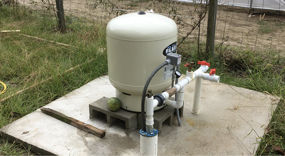 Private water well with pressure tank in grassy area near a fence.