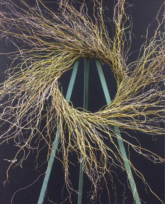 A wreath of long, twiggy stems on a wreath stand.