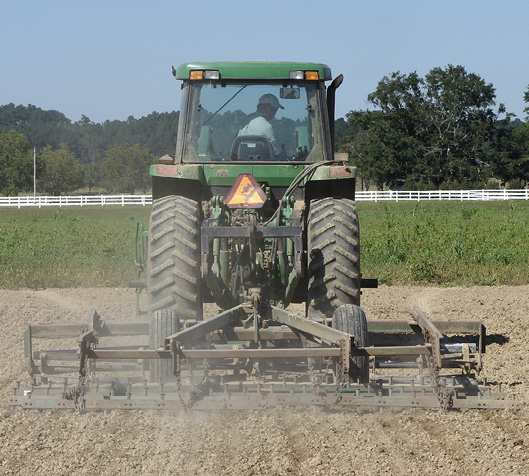 A tractor pulls an implement across a dirt field.