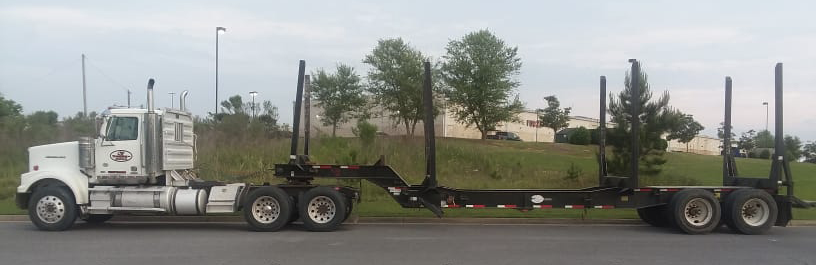 A logging truck's trailer sits empty in the parking lot.
