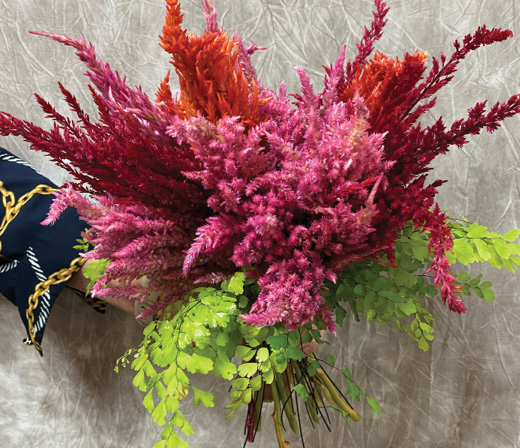 A bouquet of hot pink, dark red, and bright orange Celosia plumes and several bunches of greenery.