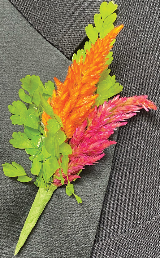 A suit lapel with a boutonniere of one hot pink and one bright orange Celosia plume, and two small bunches of greenery.