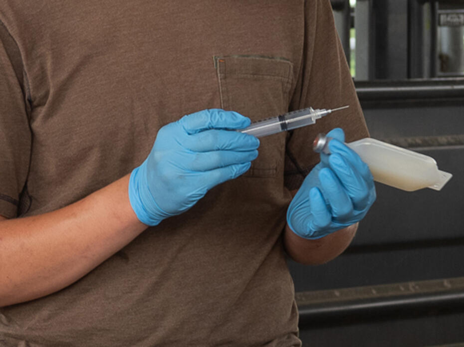 Two gloved hands hold a syringe and a medical container.