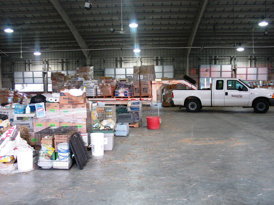 A white pickup truck inside a warehouse with boxes of household items behind it.