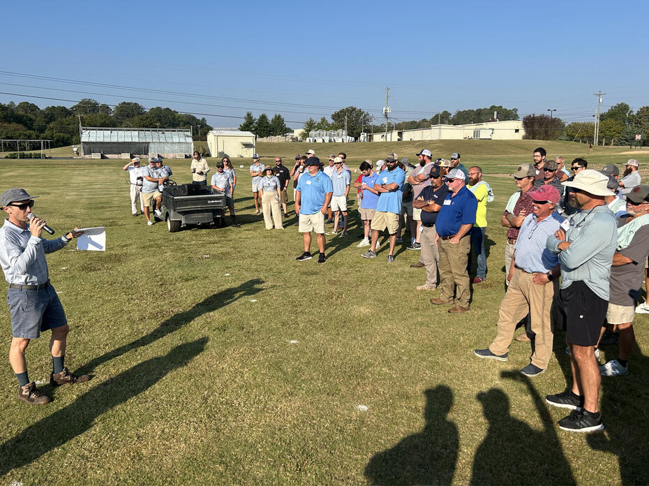 A presenter shows turf samples to a crowd of onlookers.