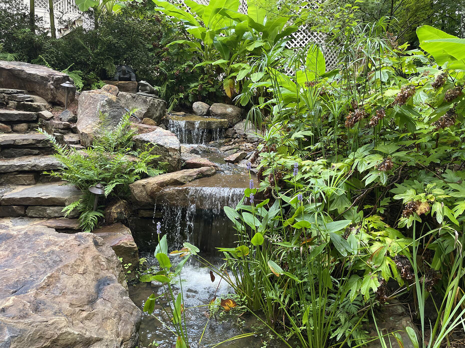 A small waterfall runs between stone steps and a lush landscape.