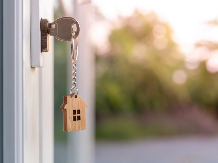 A house key on a house-shaped keychain is insterted in the front door lock of a home.