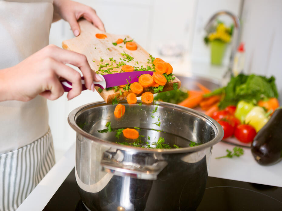 Person dumping vegetables in a pot.