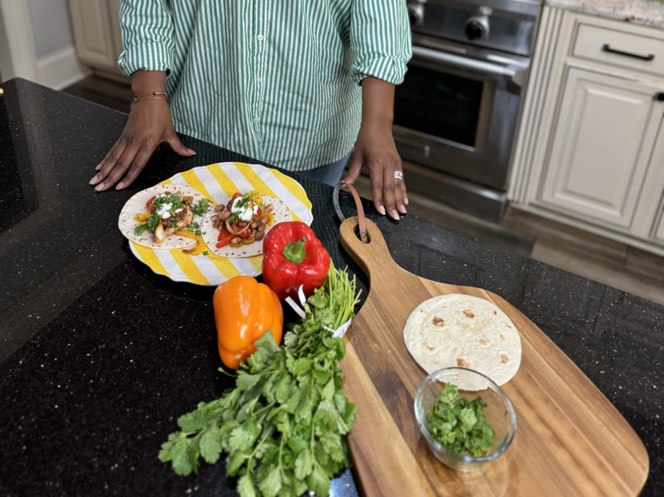 A woman in a kitchen with ingredients for fajitas on the counter.