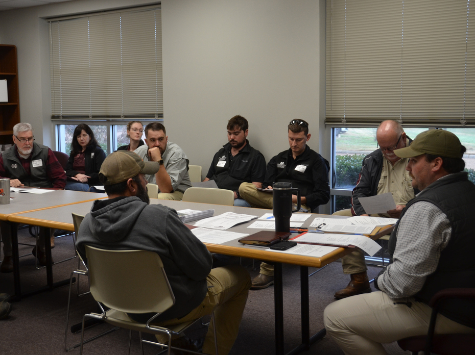 A man sits at the end of a conference room table with others gathered around.