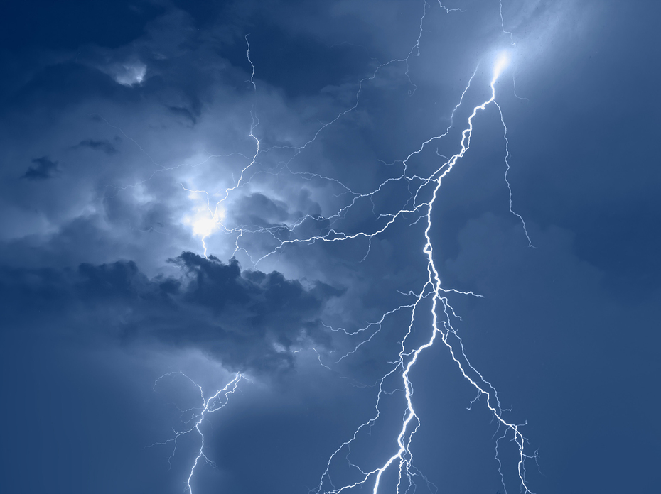 Lightning stirkes light up a cloudy, blue night sky.