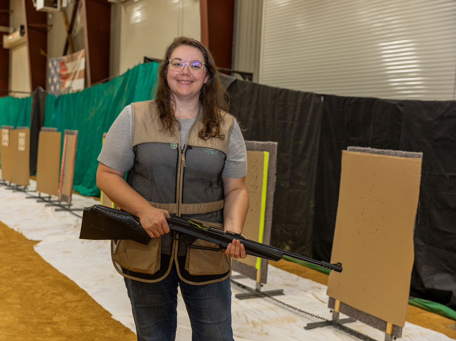 A person standing in an indoor shooting range and holding a firearm.