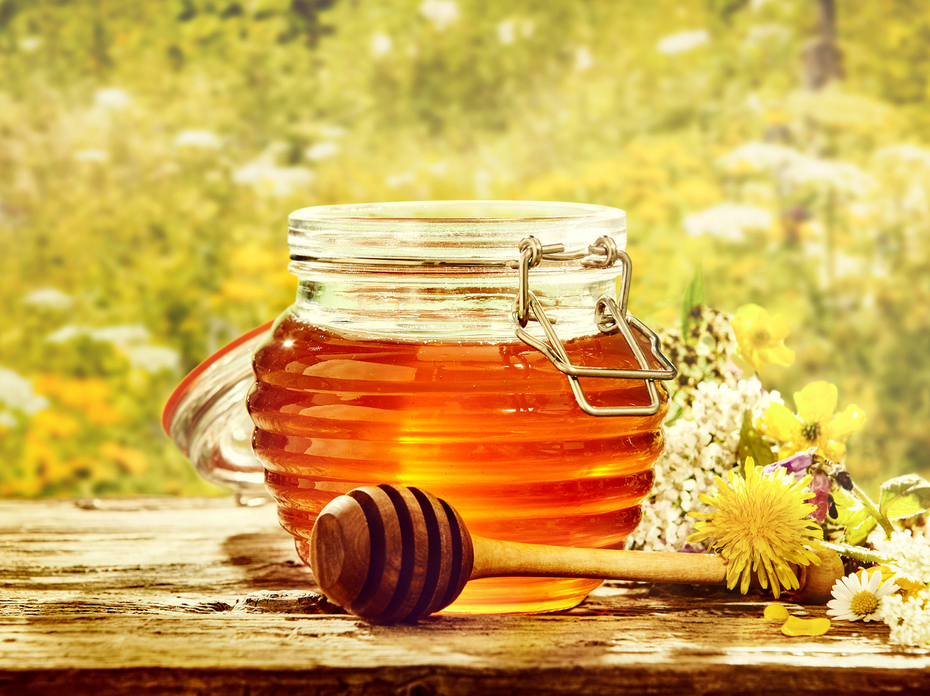 Bowl of honey with dipper in a field of flowers