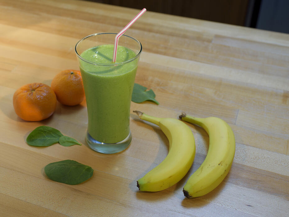 A green smoothie fills a tall clear drinking glass and has a red and white striped straw in it.  