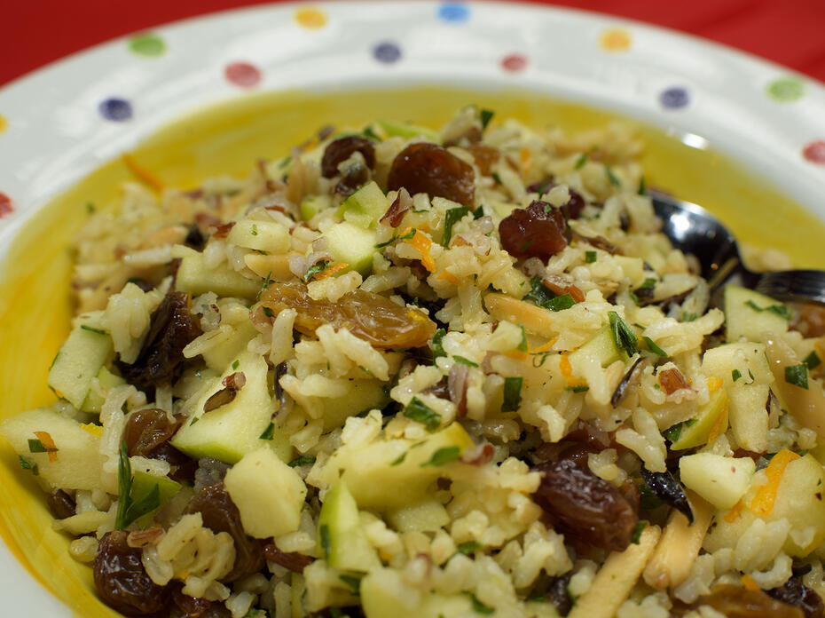 A mixture of rice, apples, raisins and almonds is displayed in a colorful bowl.