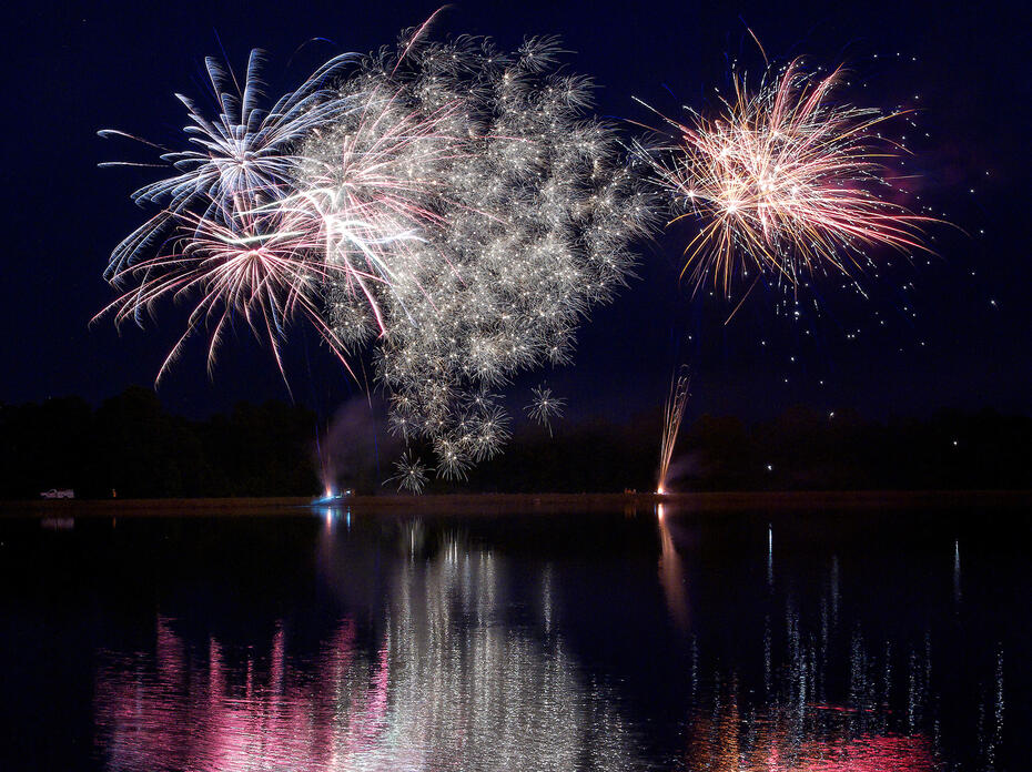 Fireworks explode against a dark sky and above a large body of water. 