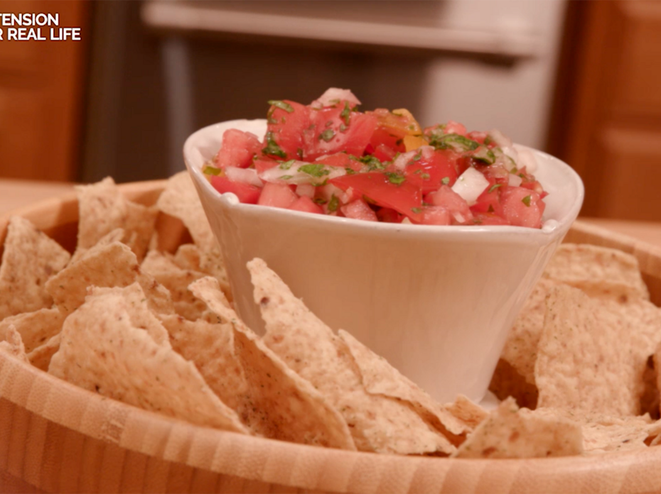 Homemade pico de gallo in a white container placed in the center of a wooden bowl of tortilla chips.