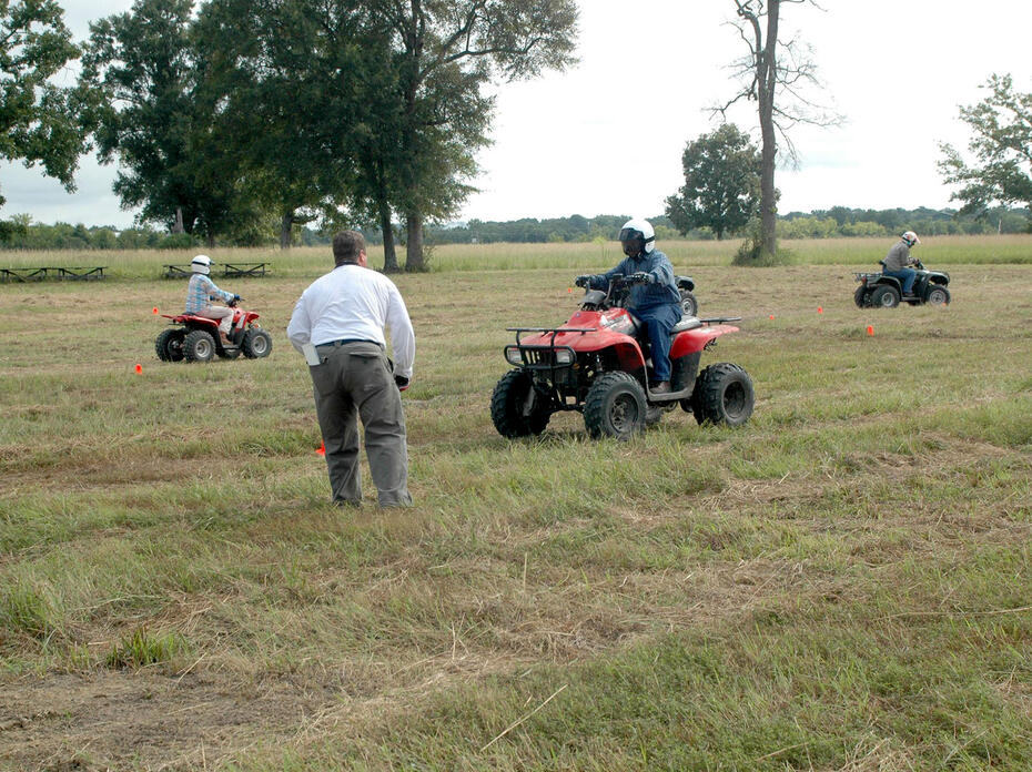 Three young people drive ATVs on a marked course in a field during a safety training.