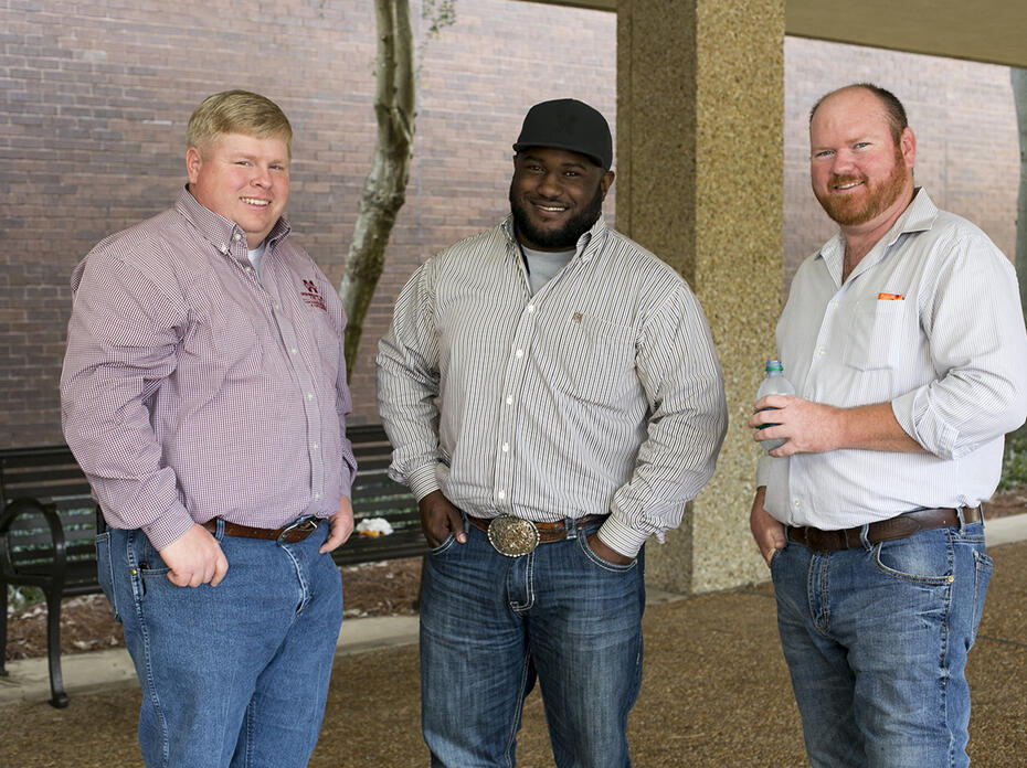 Three adult males stand outside a building.