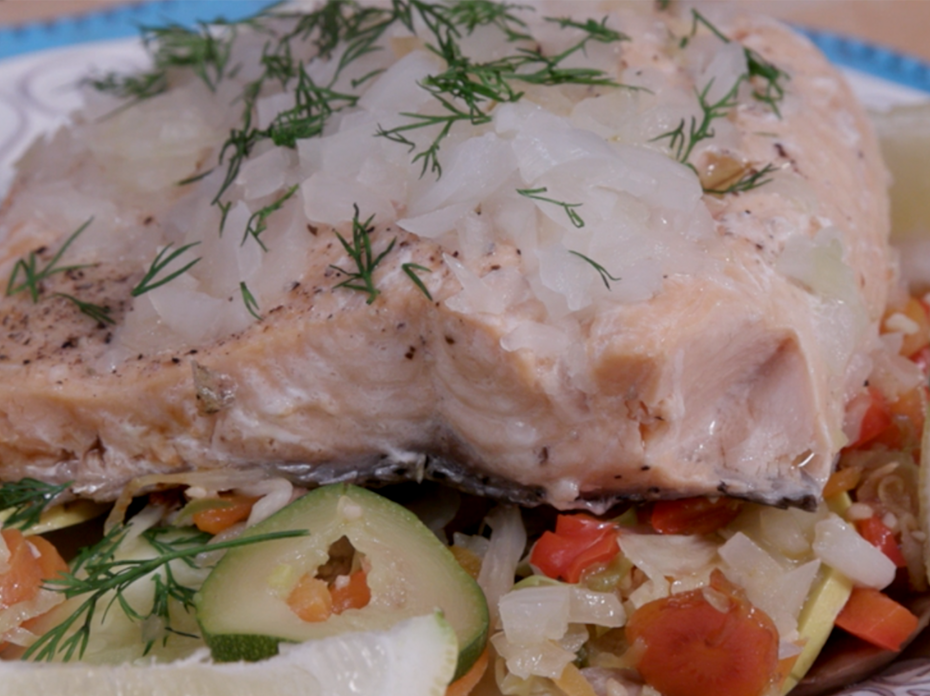 A steamed salmon filet sprinkled with onions and dill sits atop roasted vegetables. 