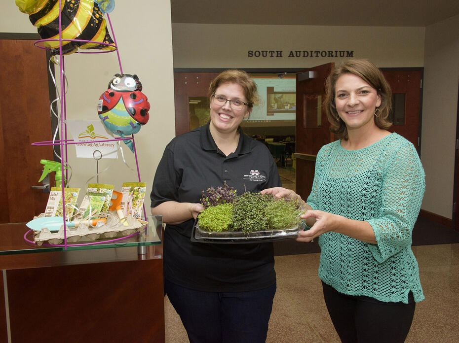 Two women hold a tray of microgreens.