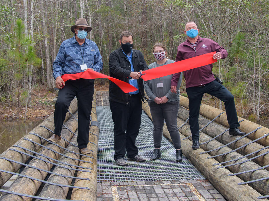 Four people stand on a bridge while cutting a ceremonial ribbon.