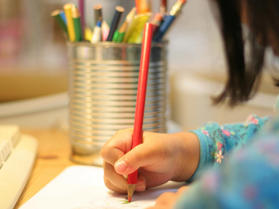 A child uses a colored pencil to write on a sheet of paper.