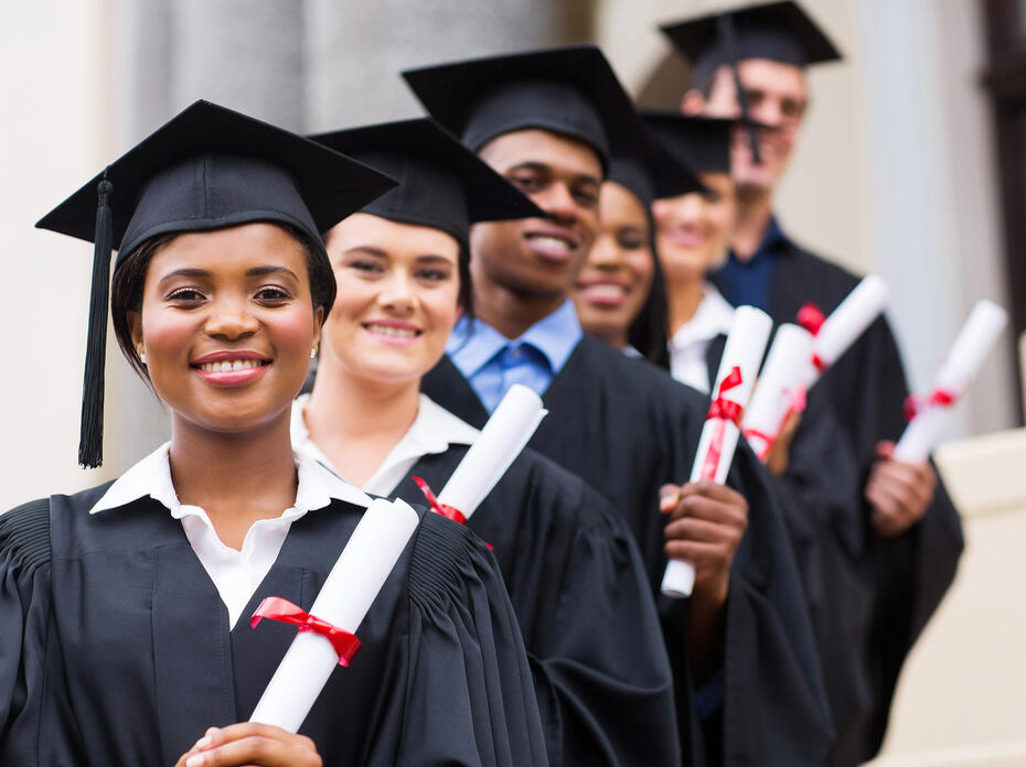 A group of smiling graduates pose in caps and gowns.