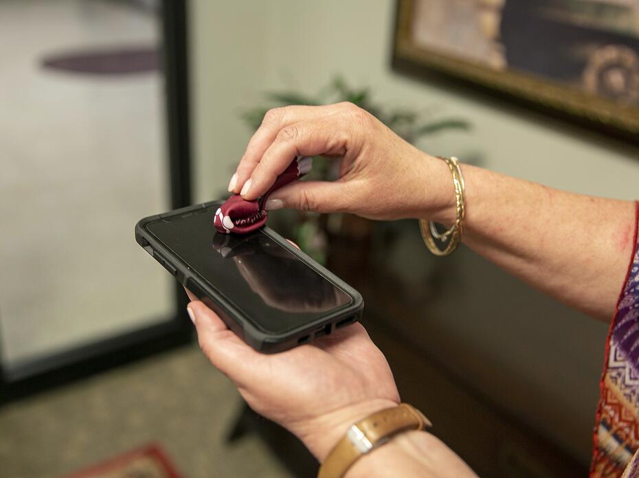 One hand holds a phone while the other hand wipes the screen with a small cloth.
