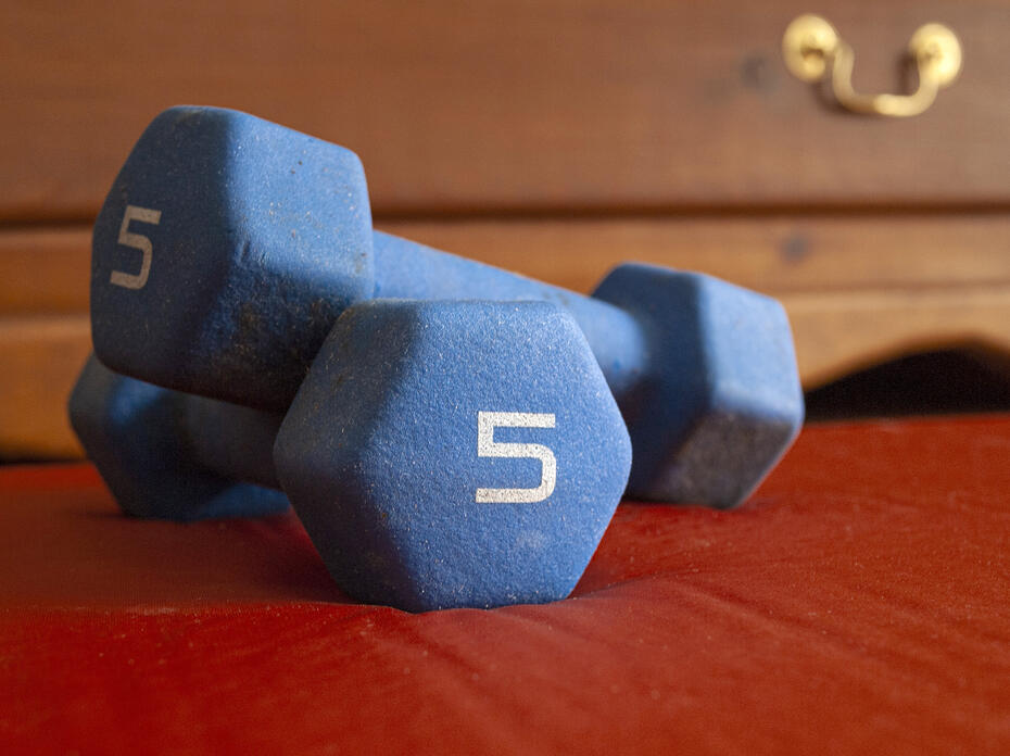 Two blue dumbbells are stacked on a bedroom floor.