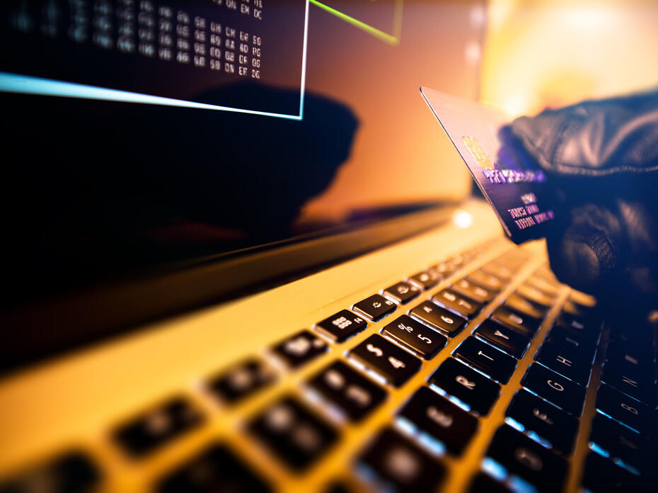 A gloved hand holds a credit card above a keyboard.