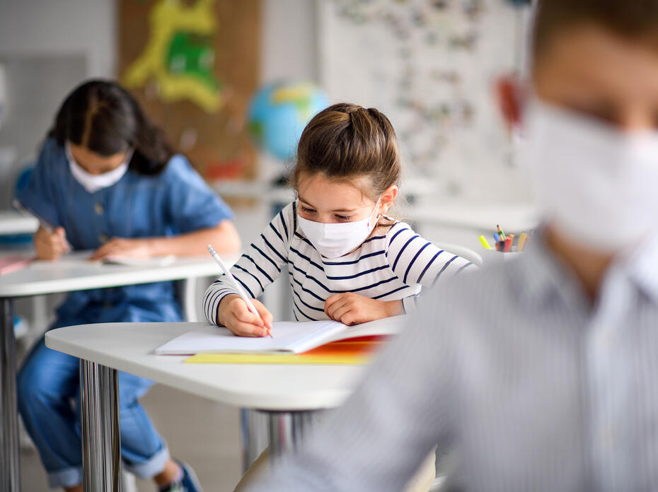 Three students wear face masks as they sit at their desks.