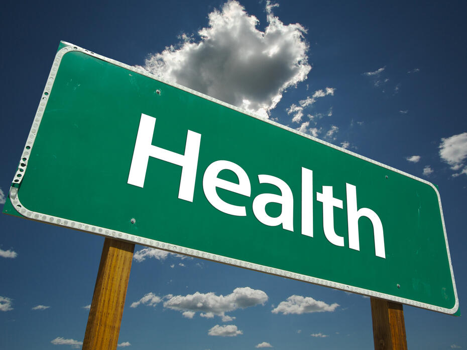 A green road sign with the word “Health” is pictured against a blue sky with white clouds.