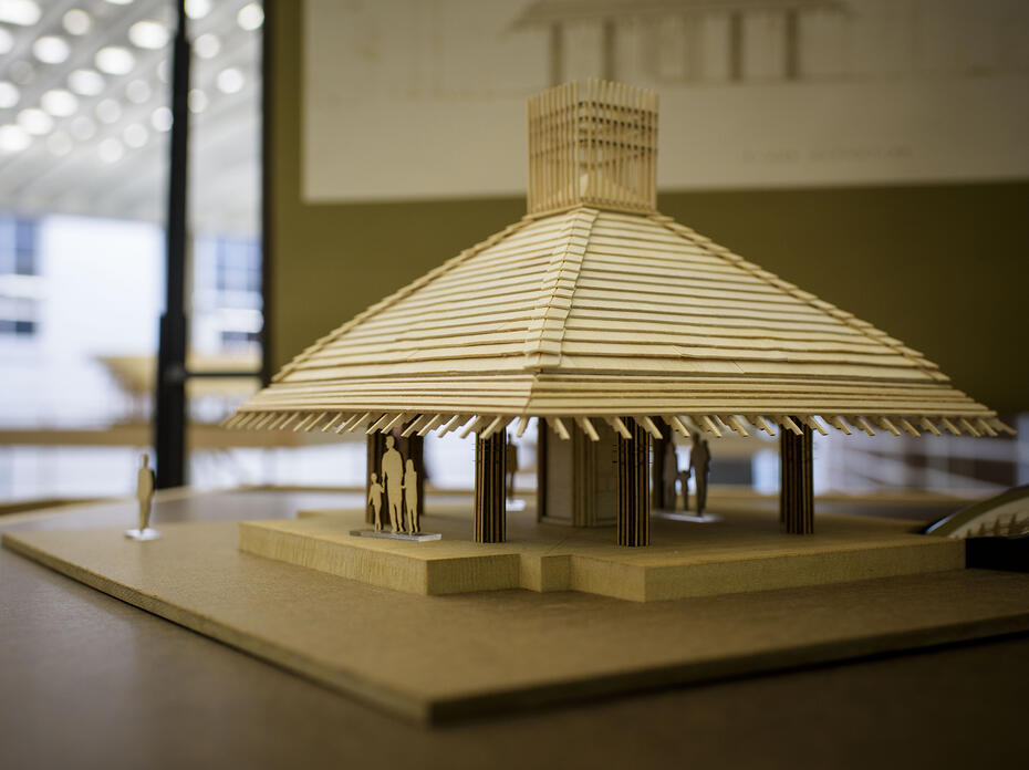 A wooden model of a building rests on a table in an exhibit hall.