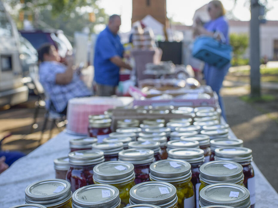 Rows of canning jars line a table at an open-air marketplace.
