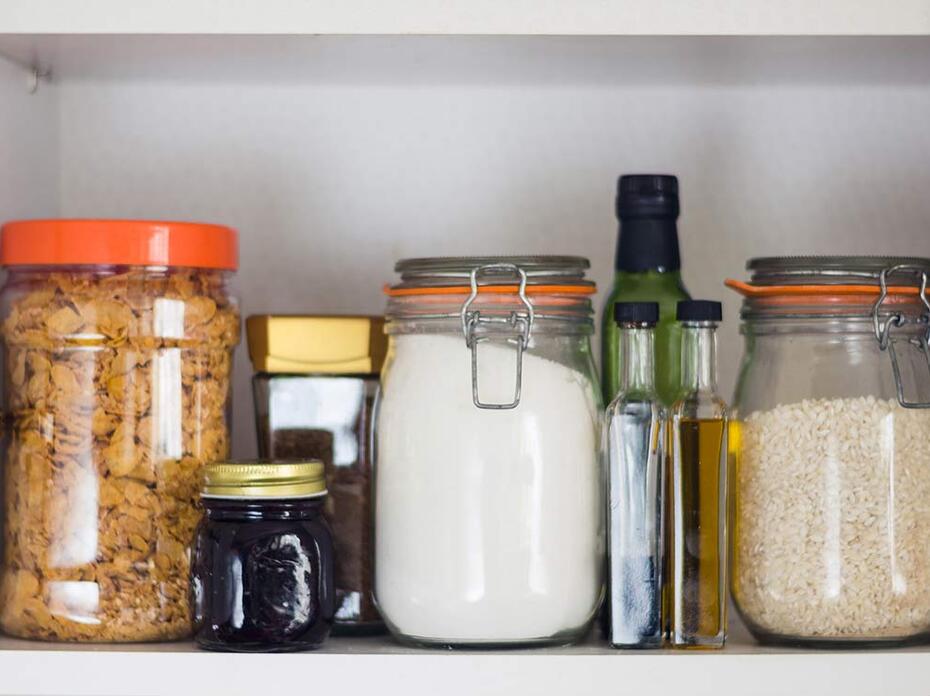 Airtight jars of cereal, rice and flour sit in a cupboard.