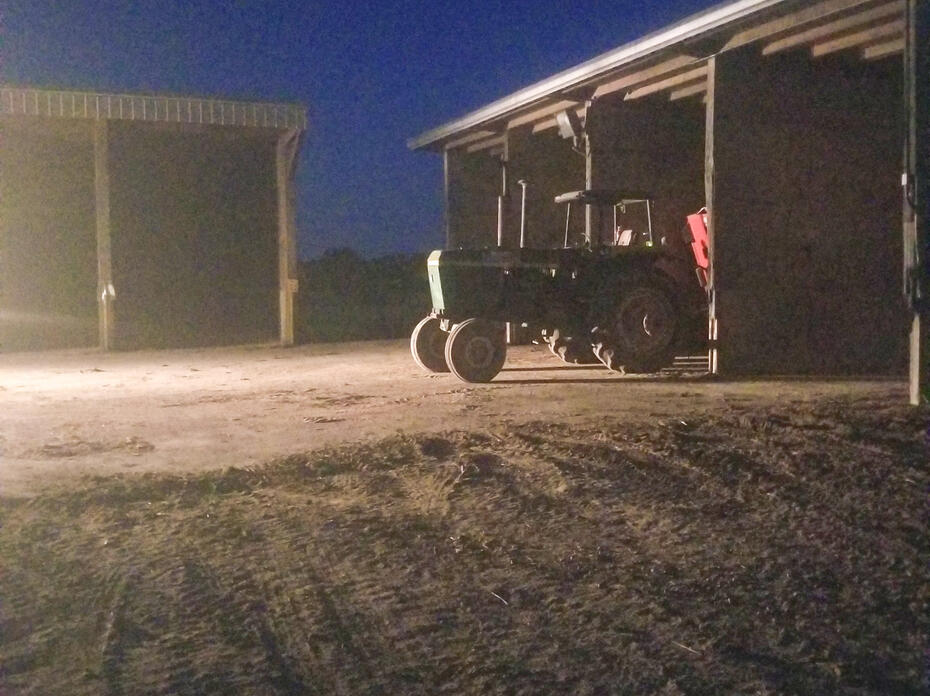 A tractor parked outside of a shed at night.