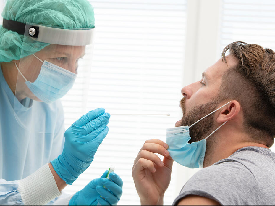 Medical worker in protective clothing takes a throat swab from a male patient.