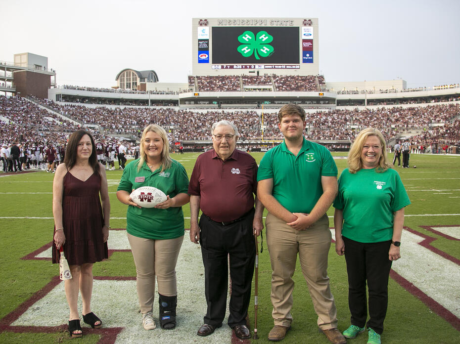 Five people pose for a photo on a football field.